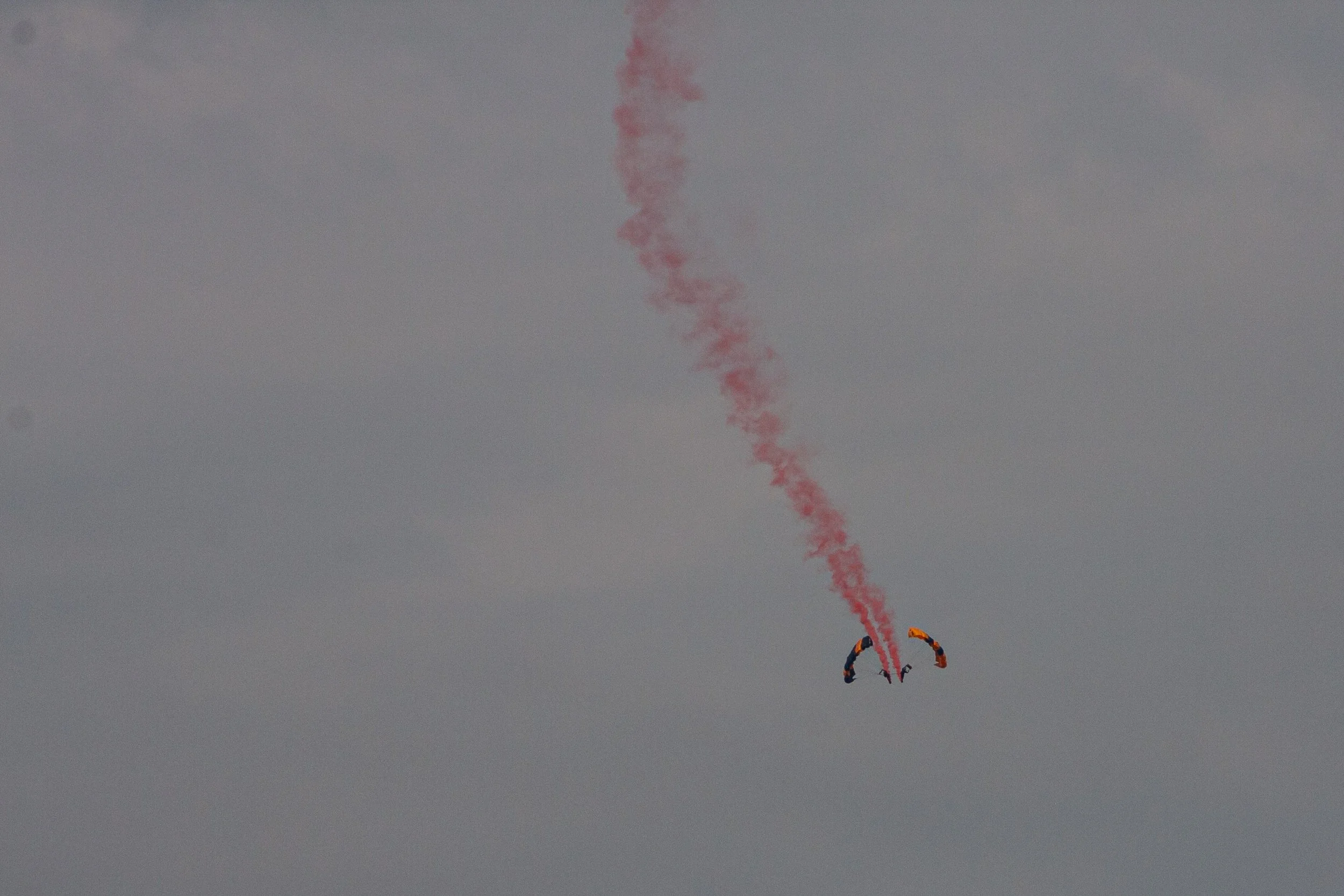 An aerobatic aircraft leaves a curling red smoke trail.