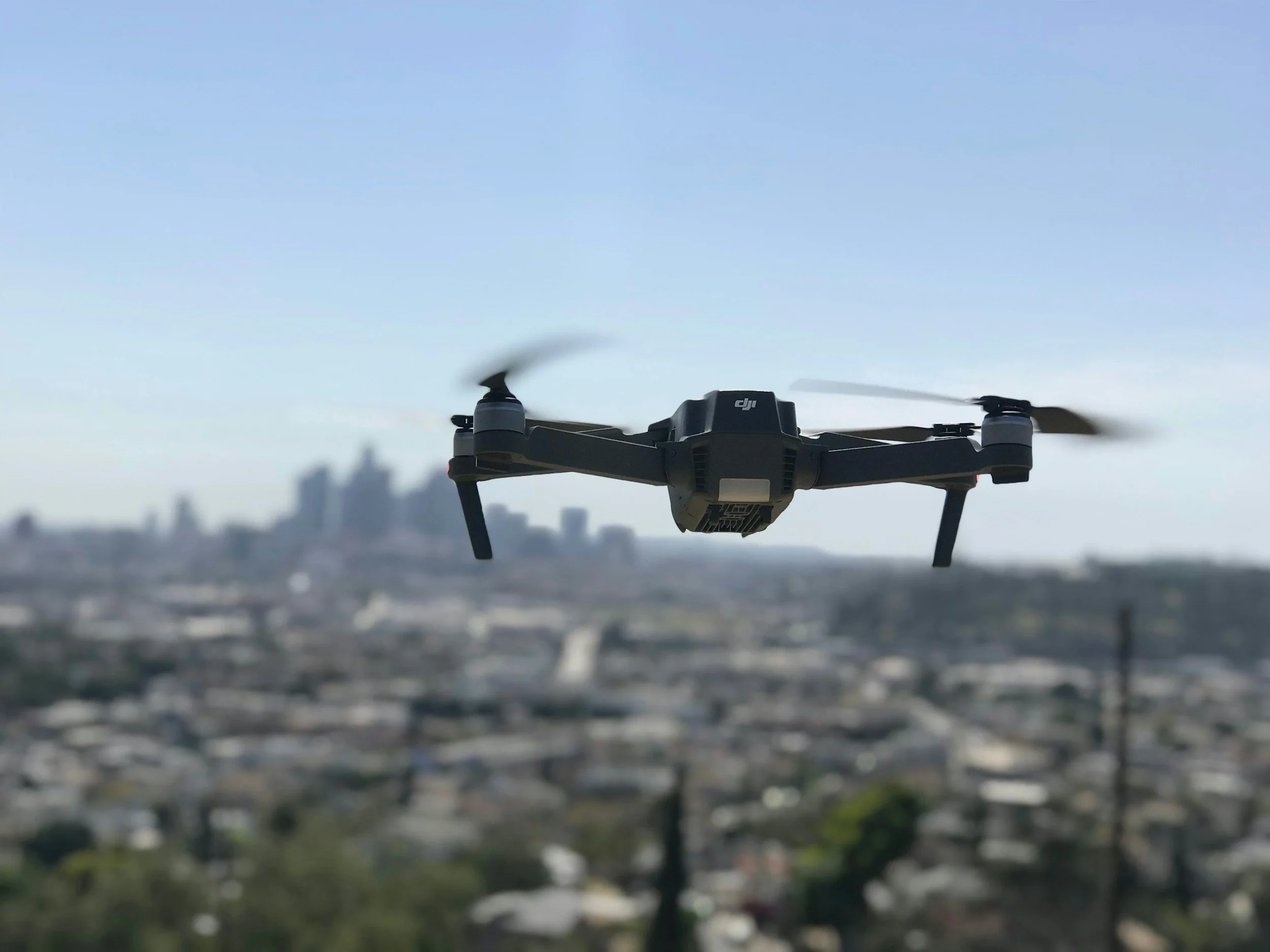 A DJI drone flying over a cityscape with blurred buildings in the background.