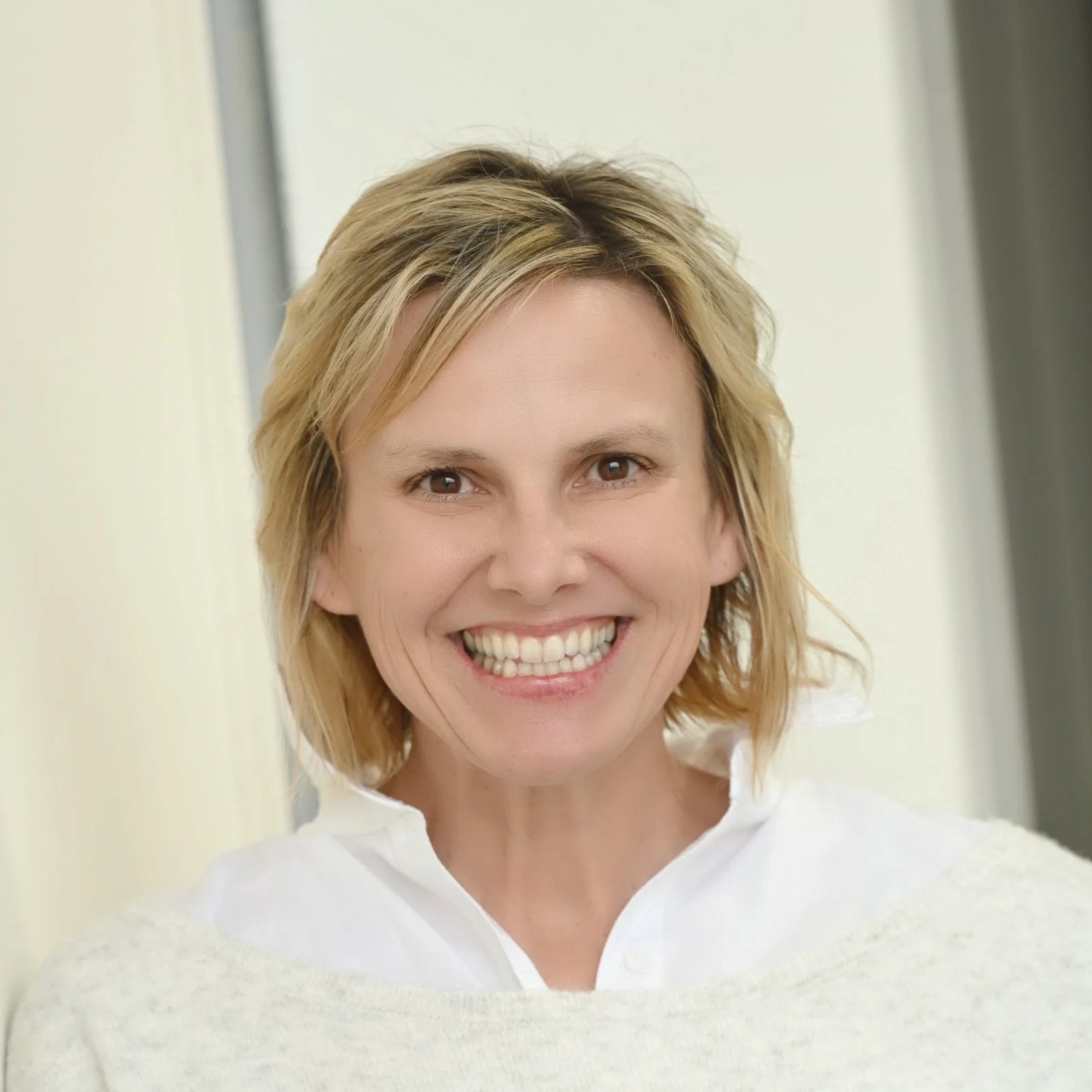 A woman with blonde hair smiling and wearing a white top.