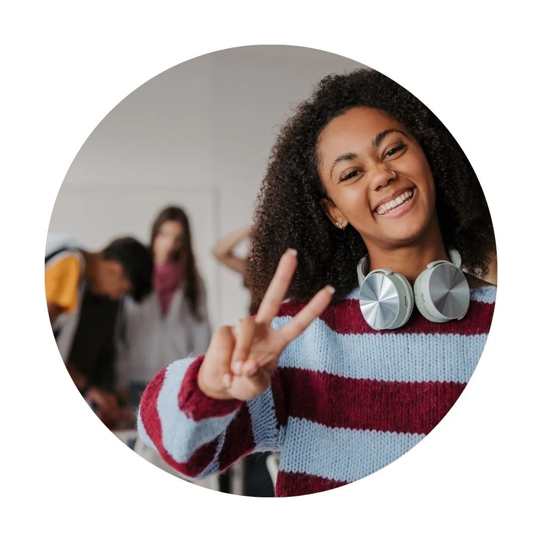 Smiling teenager with headphones around their neck holding up a peace sign, representing supportive therapy for teens in Dallas, TX.