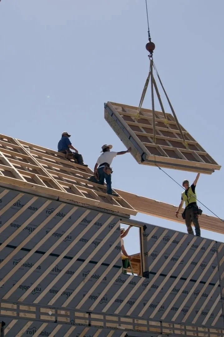 Construction workers installing roof panels on a building under clear sky.