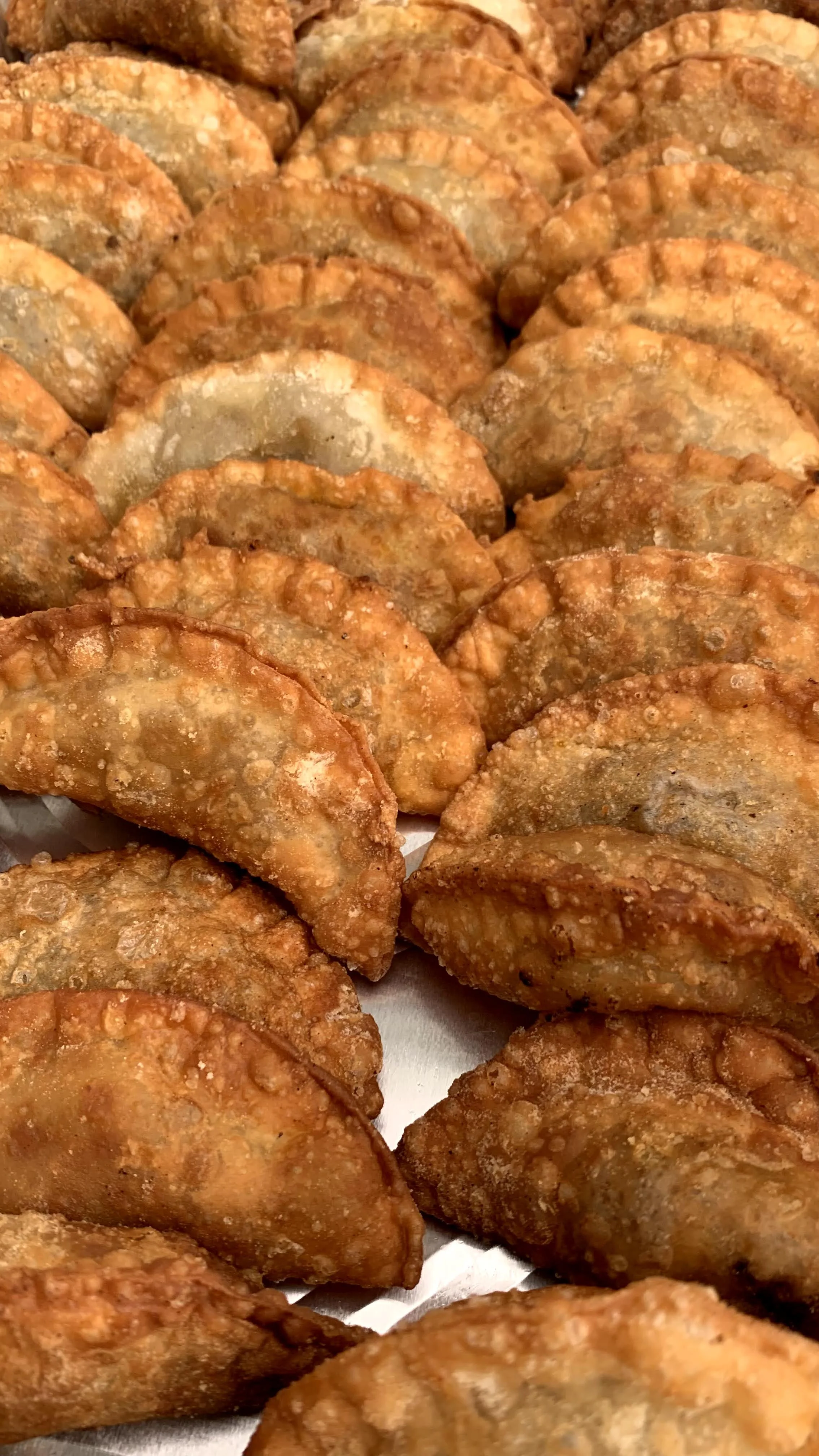 Close-up of crispy, fried empanadas with a golden-brown exterior arranged in rows.