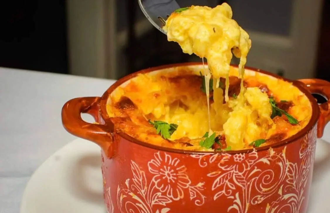A bowl of baked macaroni and cheese with cheese and parsley garnished.