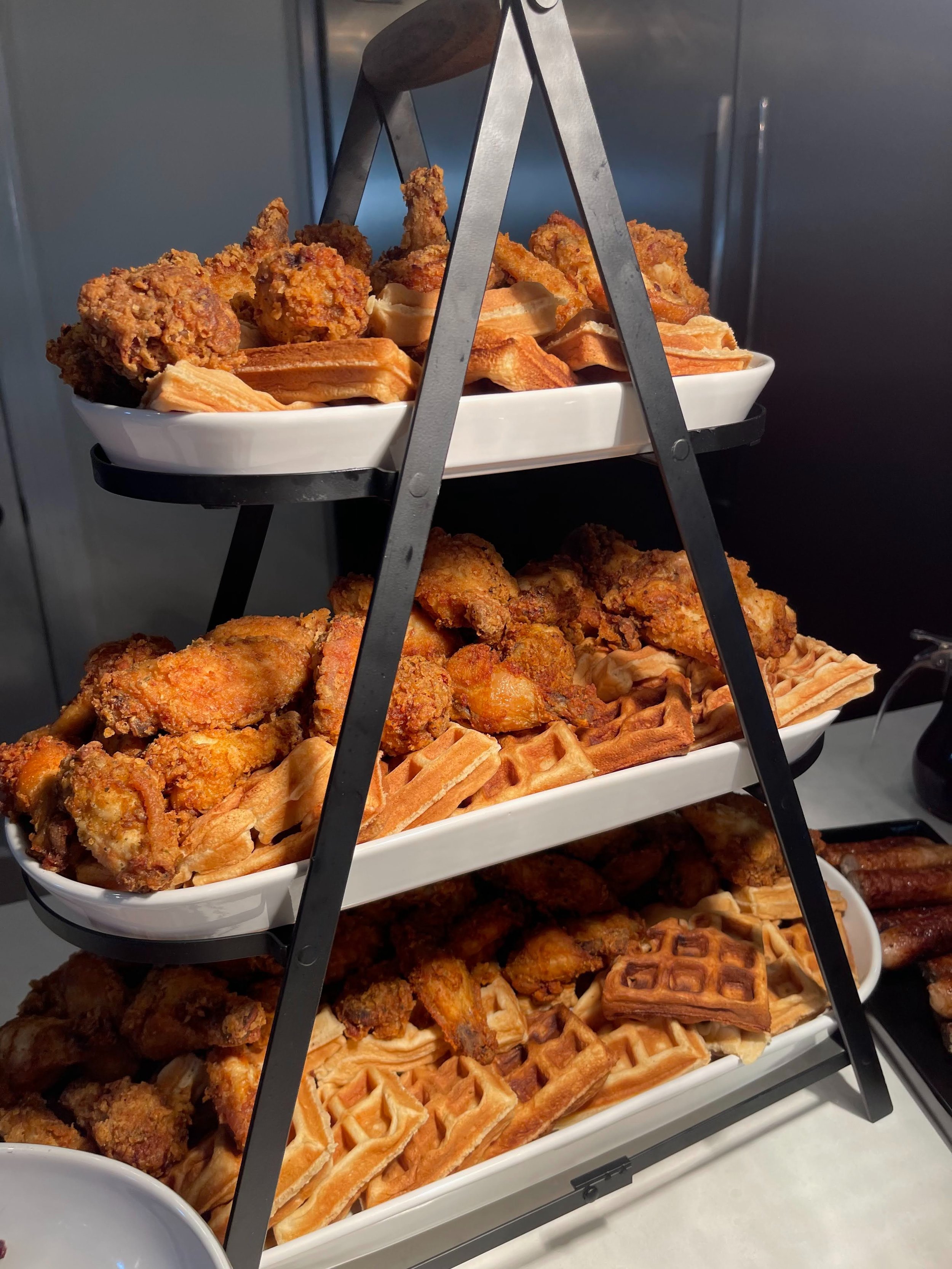 Three-tiered serving rack filled with fried chicken and waffles.