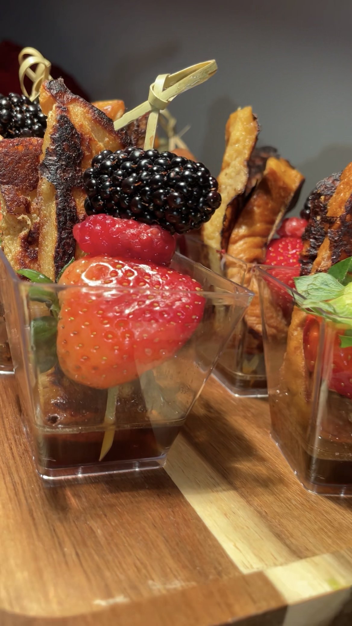 Close-up of fruit and French toast stick served in small containers with syrup on a wooden board.