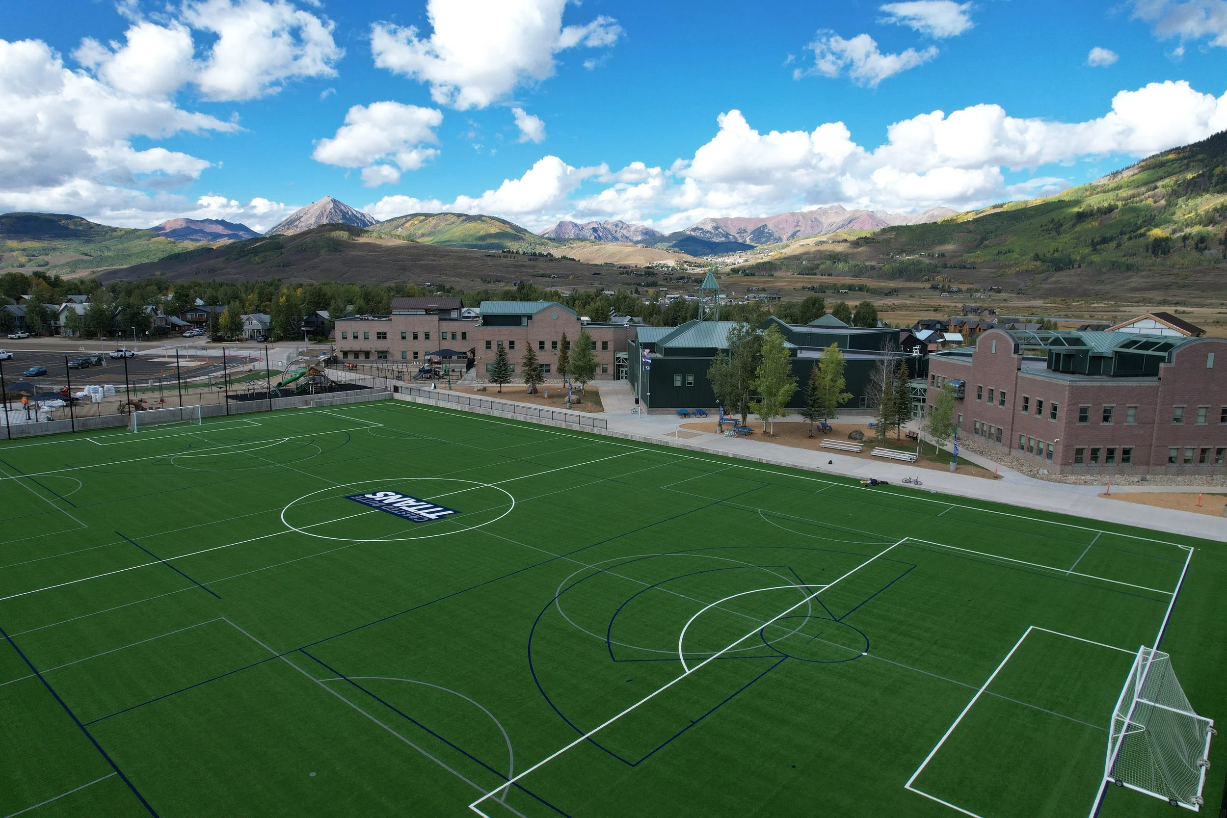 Exterior of a modern multi-story building with a curved entrance, black vertical panels, and a sign reading 'The Pinnacle.' Tall high-rise buildings are in the background against a partly cloudy sky.