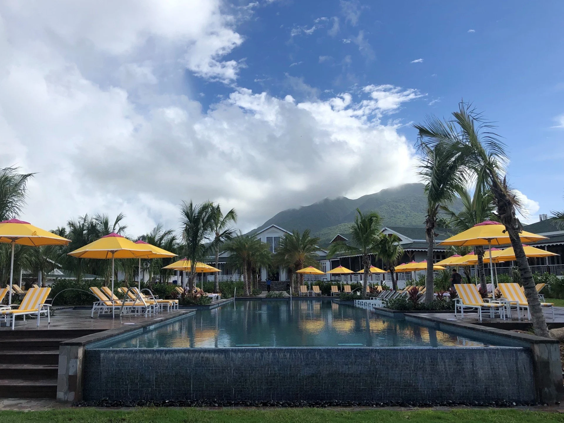 A modern three-story apartment building with a combination of dark gray, wood, and stone exterior. It features multiple balconies and garage doors on the ground level, with a clear blue sky in the background.