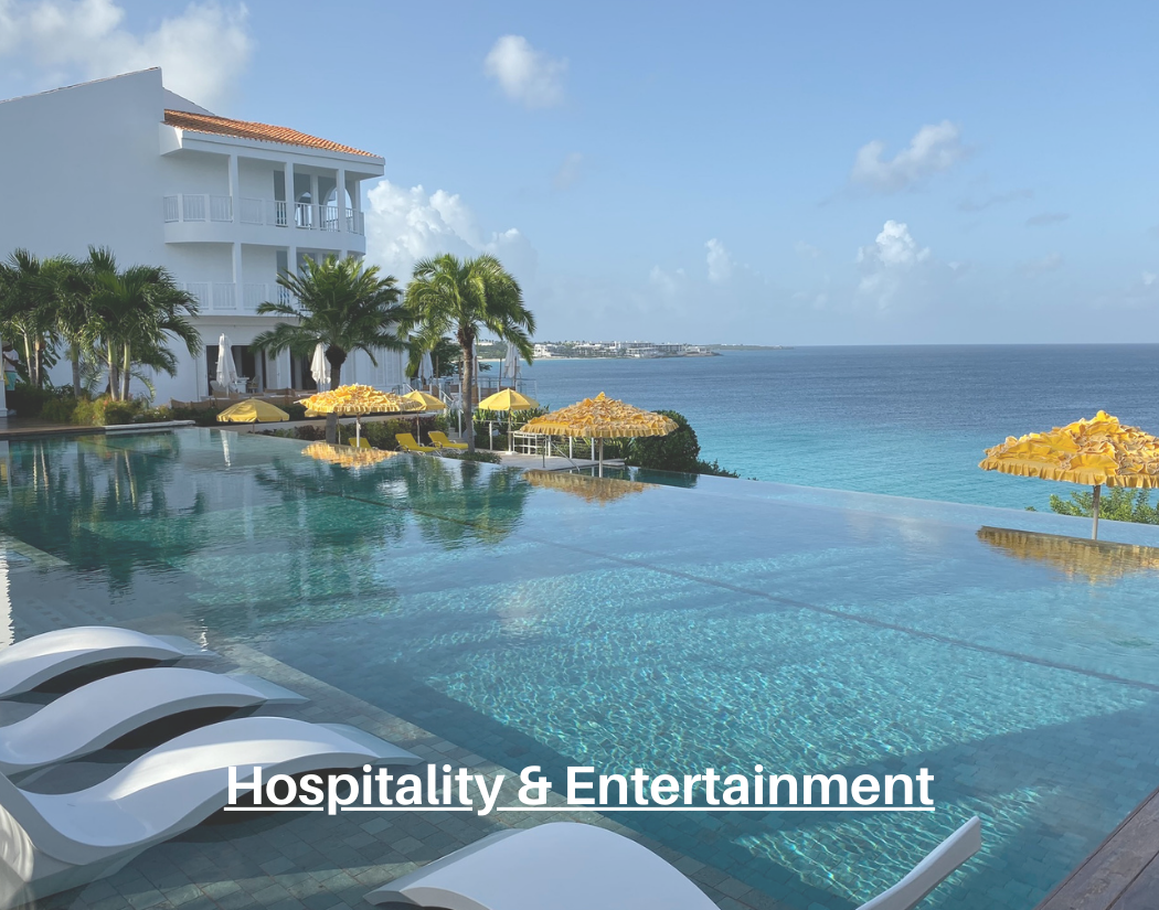 Luxury resort with an infinity pool overlooking the ocean, surrounded by lounge chairs with yellow umbrellas, palm trees, and a white building with balconies.