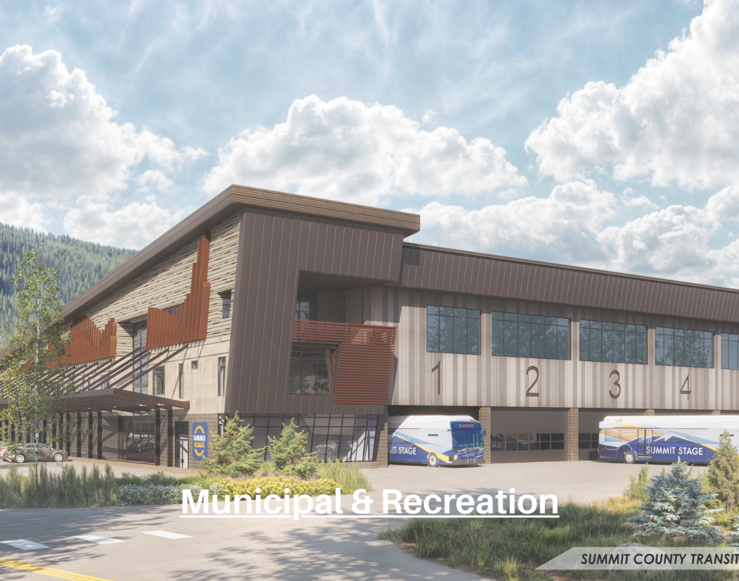 Modern municipal and recreation building with parking area, buses, and landscaping under a partly cloudy sky.