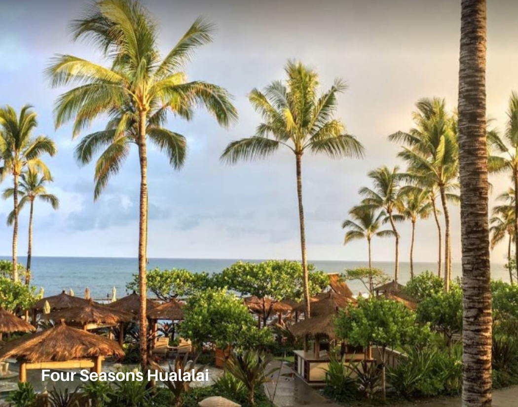 Tropical beach scene with tall palm trees, thatched-roof huts, and the ocean in the background, labeled 'Four Seasons Hualalai'.