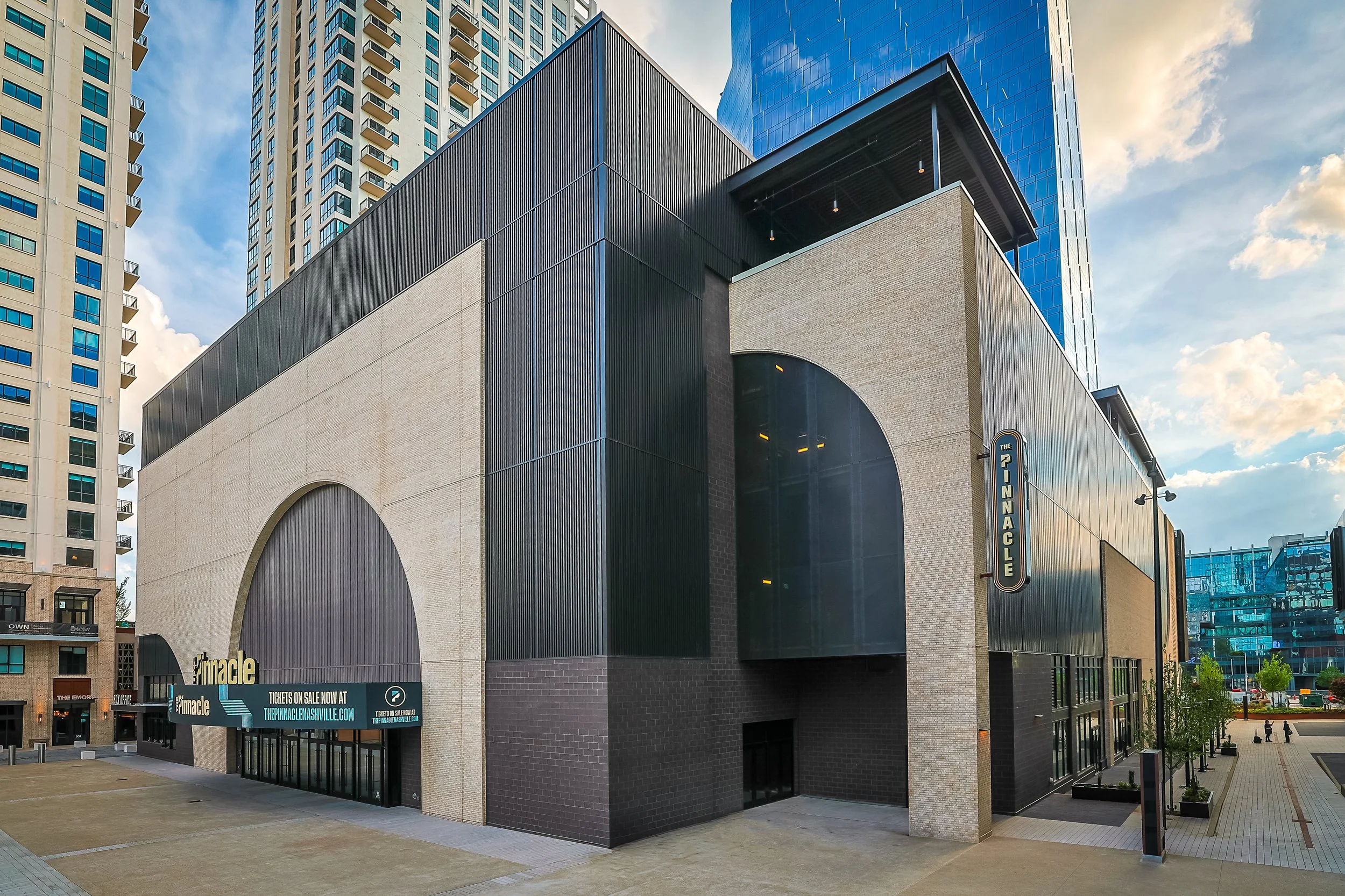 An aerial view of a sports field with a building and parking lot in the background, surrounded by mountainous terrain and a partly cloudy sky.