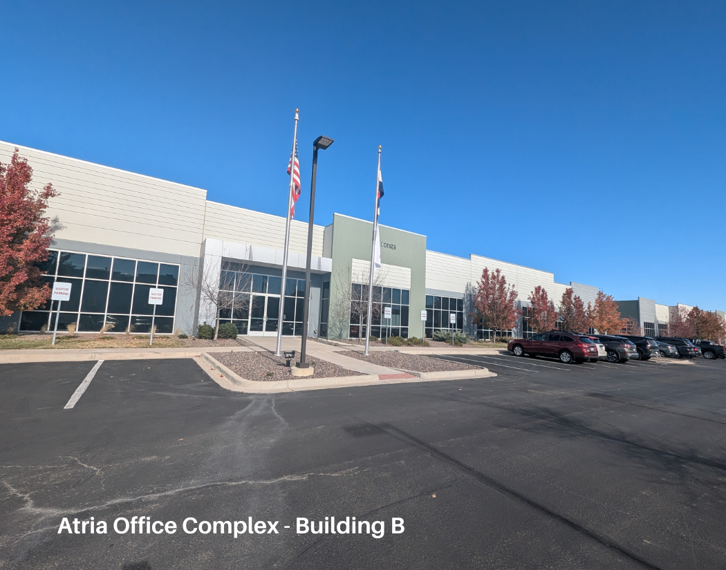 A modern office building with a parking lot, American and Texas flags, and a few trees with fall foliage in front.