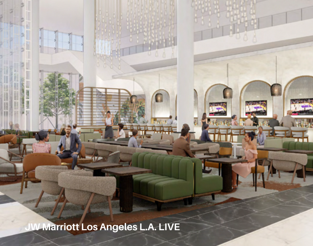 Interior of a modern hotel lobby with green and beige seating, a bar area in the background with people, large windows, and decorative hanging light fixtures.