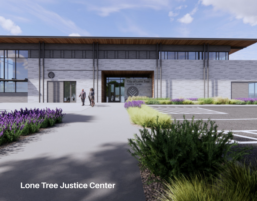 Front view of the Lone Tree Justice Center with people walking towards the entrance, surrounded by landscaped bushes and flowers under a partly cloudy sky.