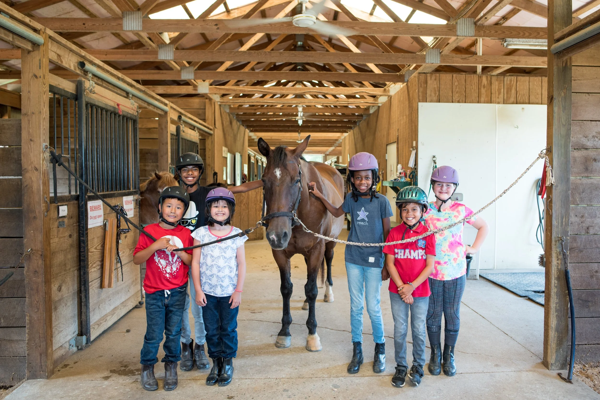 The students in riding gear smile beside one of Oakland's kind horses.