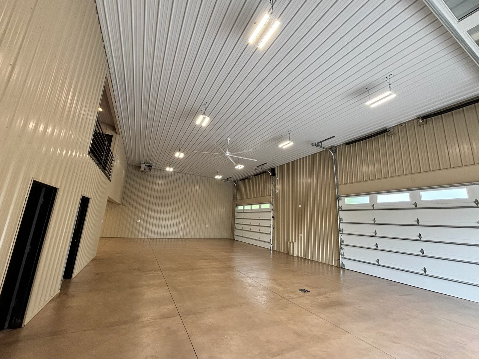 Interior of a spacious garage with beige metal walls and ceiling, concrete floor, and three large white garage doors with windows.