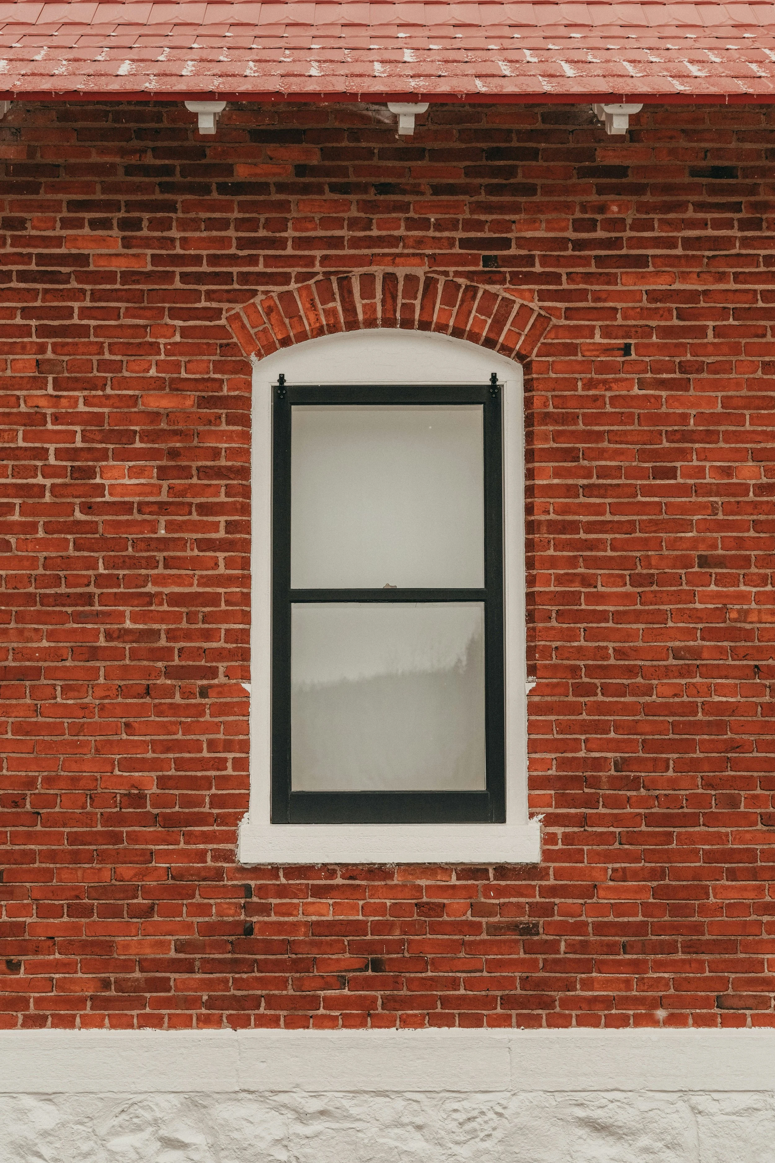A red brick building with a white-framed window and black trim, and a tiled roof.