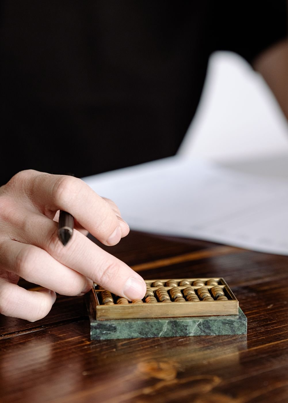 A close up of a bookkeeper's hand balancing books using a vintage marble and brass abacus.