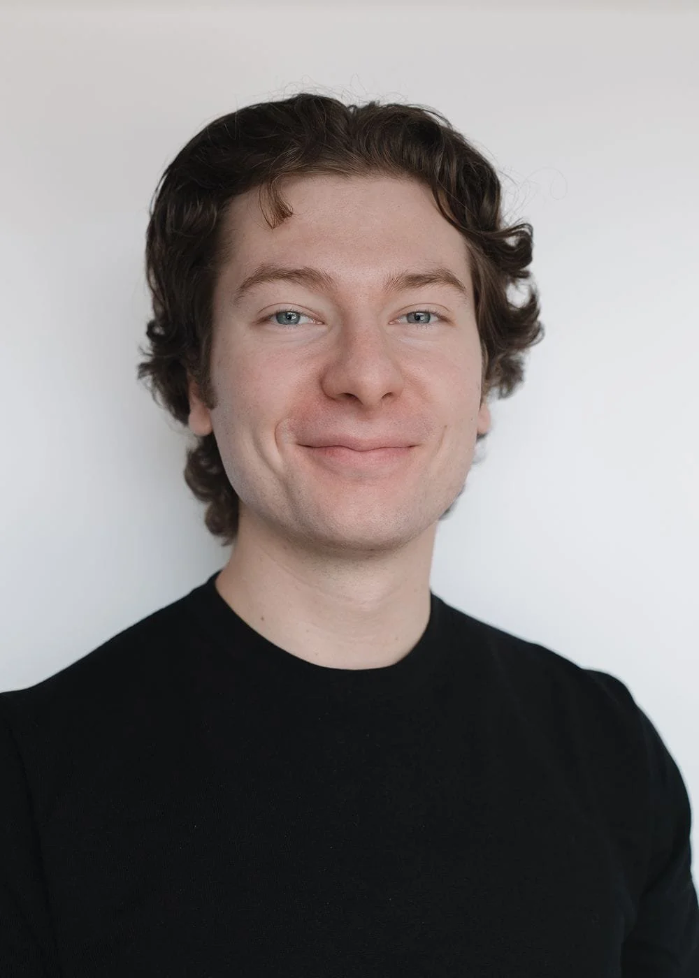 A headshot of Henry True, the founder and independent bookkeeper of TrueBooks. He is smiling, wears a black shirt, has brown hair and stands in front of a white wall.