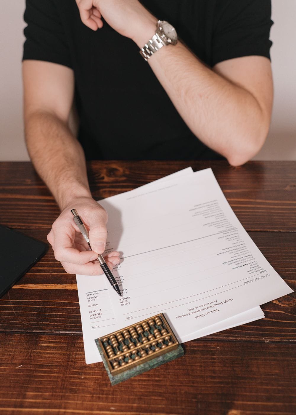 A top down photo of a bookkeeper's profit and loss statement for a client. A marble and brass abacus sits near the papers.