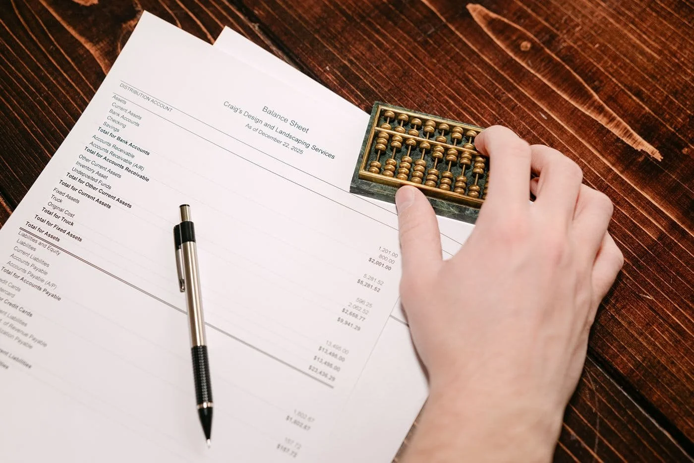A close up of a bookkeeper's hand balancing a ledger with an abacus.