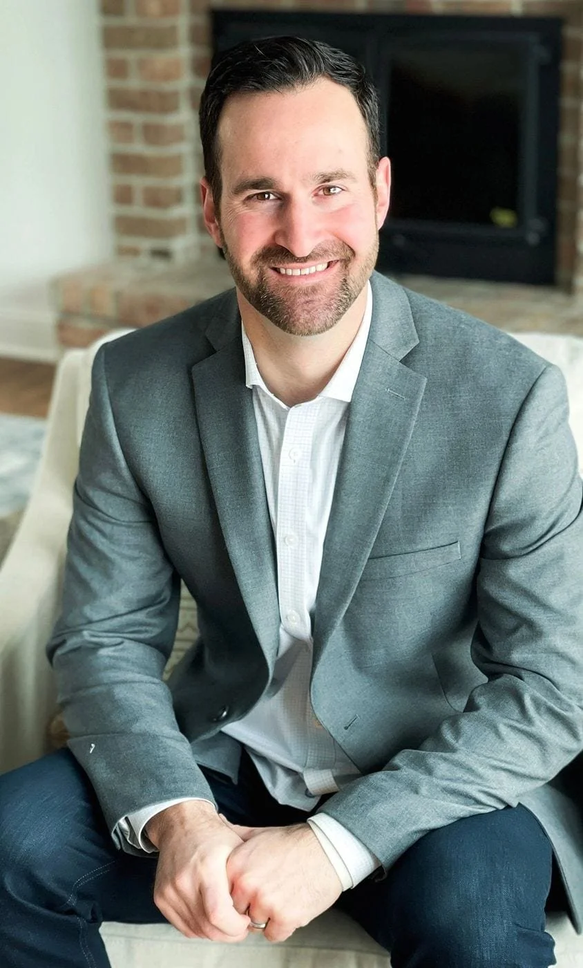 A headshot of a man in his Accounting office. He is smiling, has black hair, and is wearing a blue/gray suit.