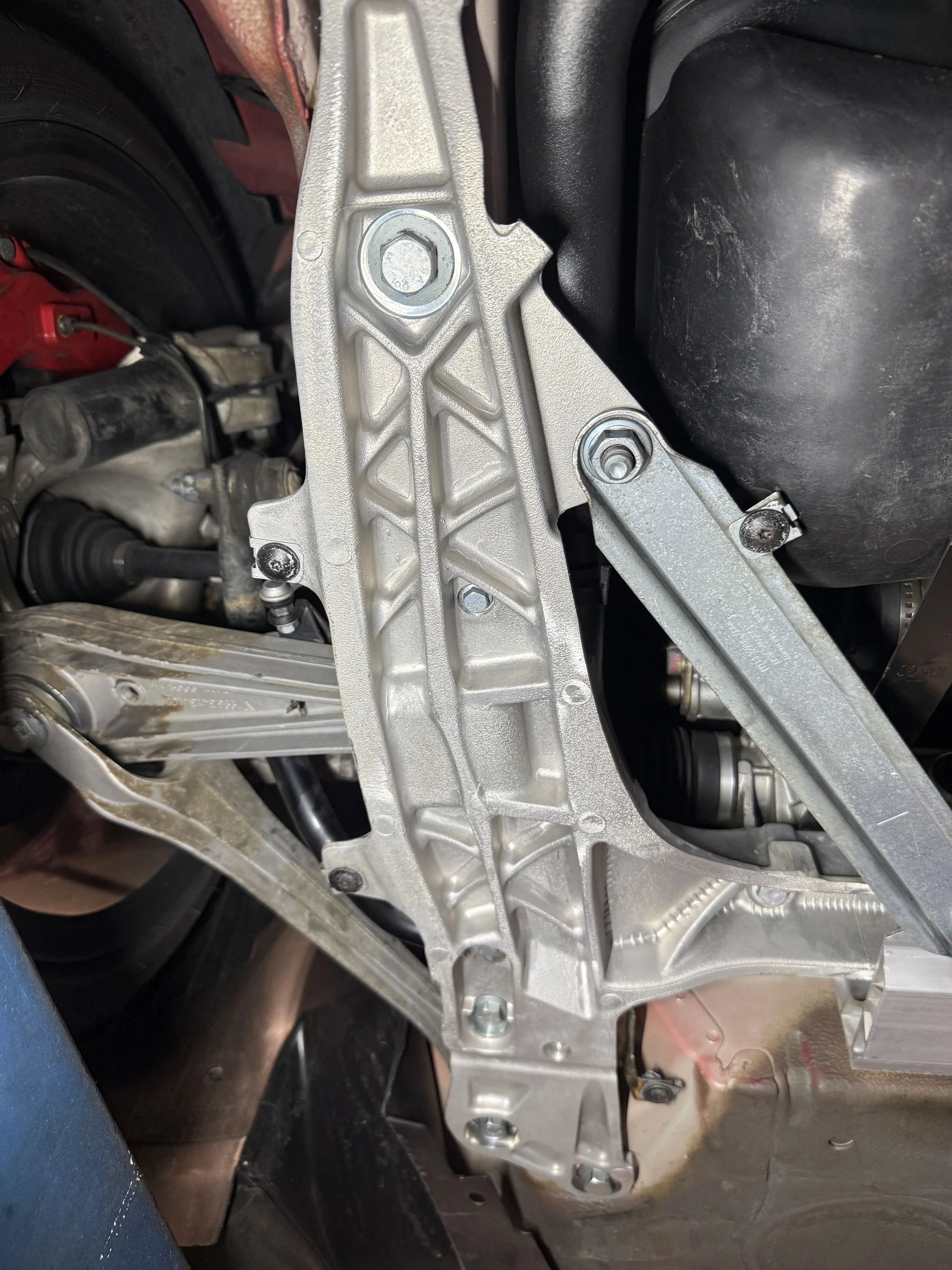 Close-up view of a car's chassis showing a metallic structure, with bolts and engine components visible around it.