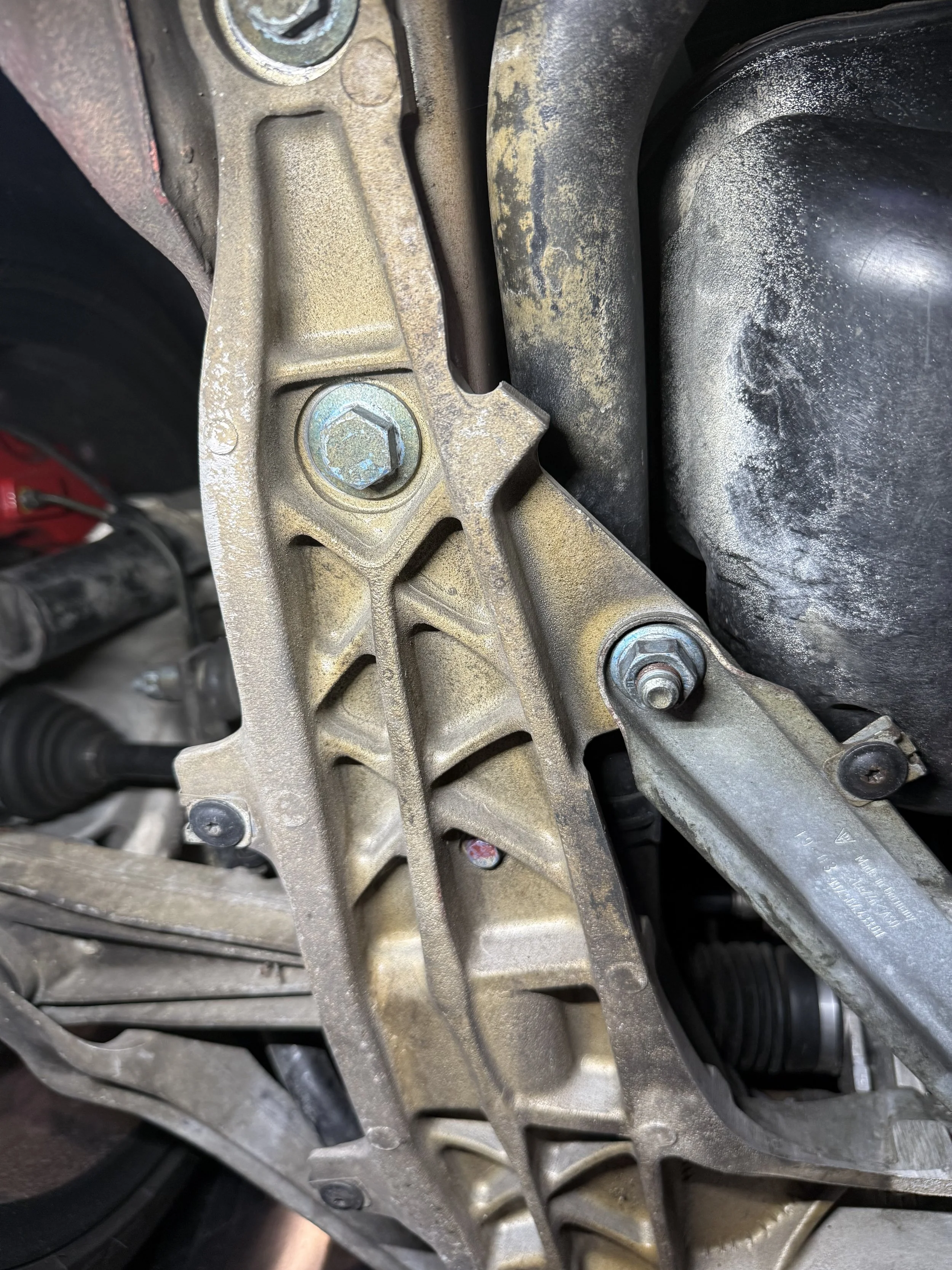 Close-up view of part of a vehicle's engine or transmission assembly, showing metallic components, bolts, and a black rubber hose.