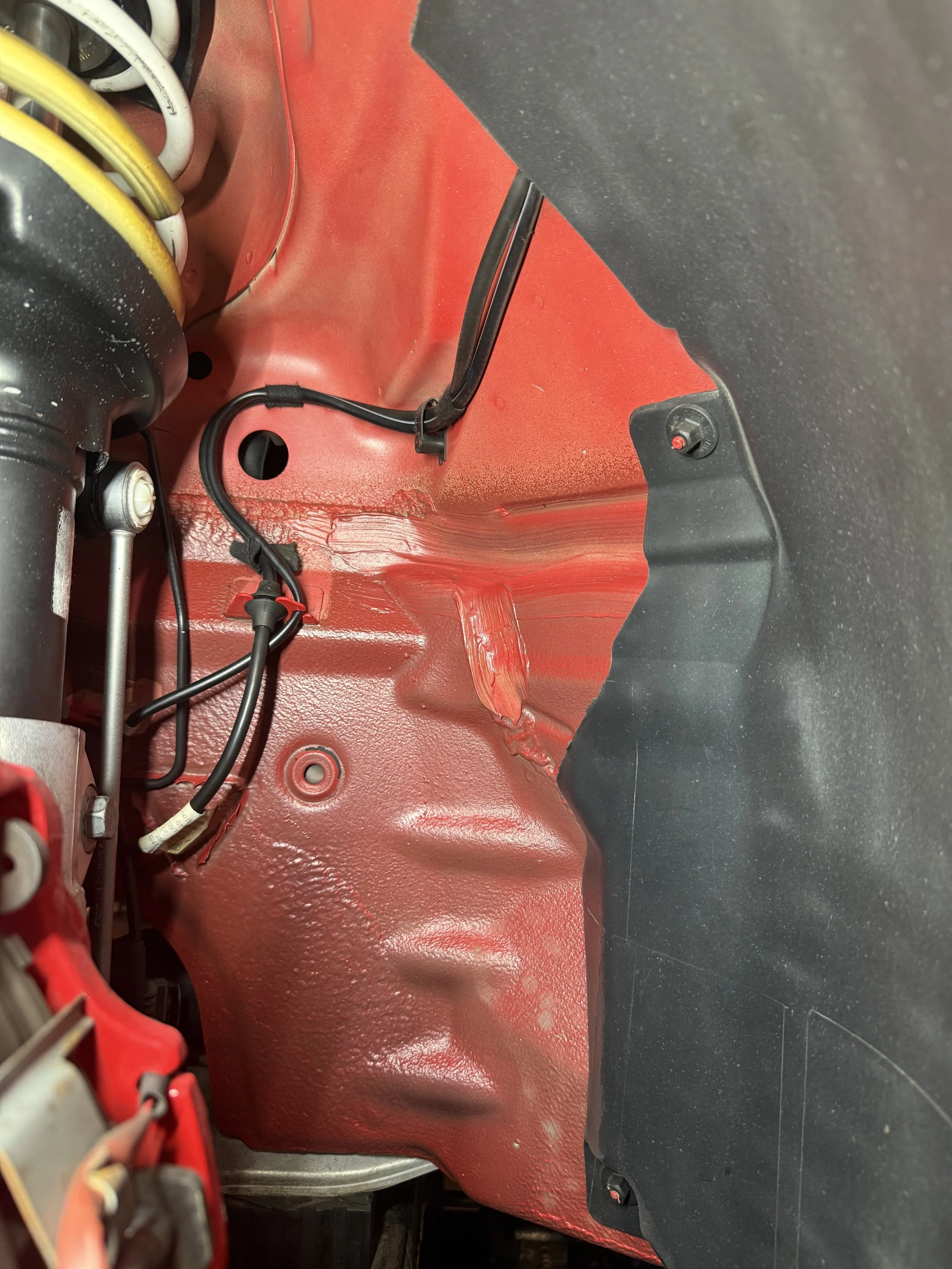 Close-up of the interior fender area of a car with red painted metal, wires, and a black plastic lining.