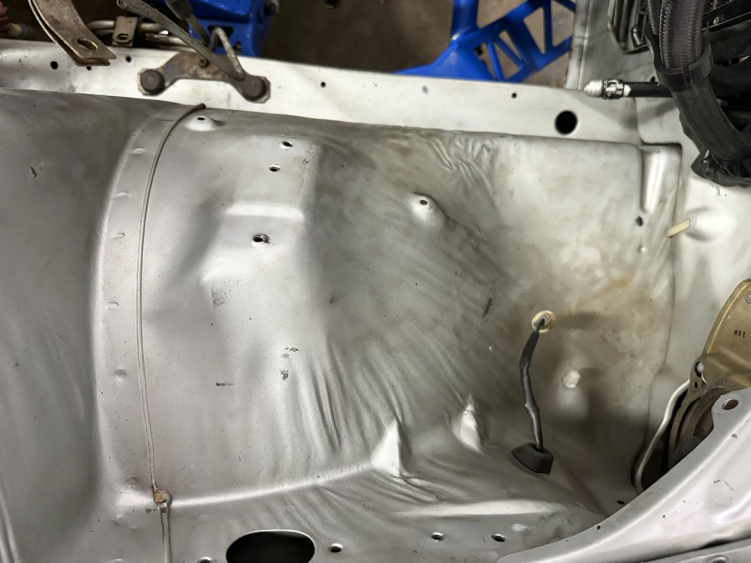 Empty car engine bay with visible wiring and mounting points, with some dirt and minor rust spots.