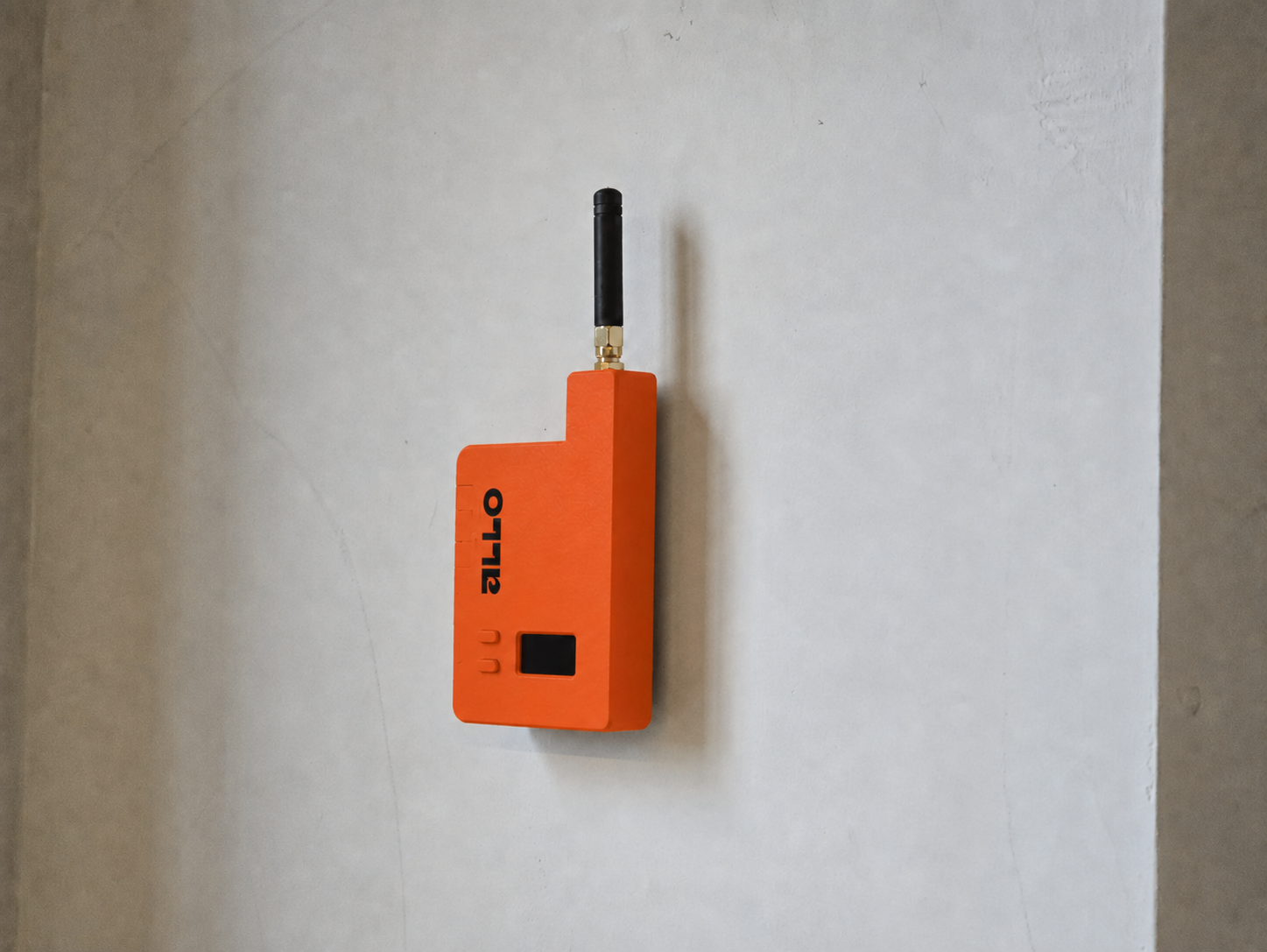 Een oranje apparaat met een zwart antenne, op een witte muur.