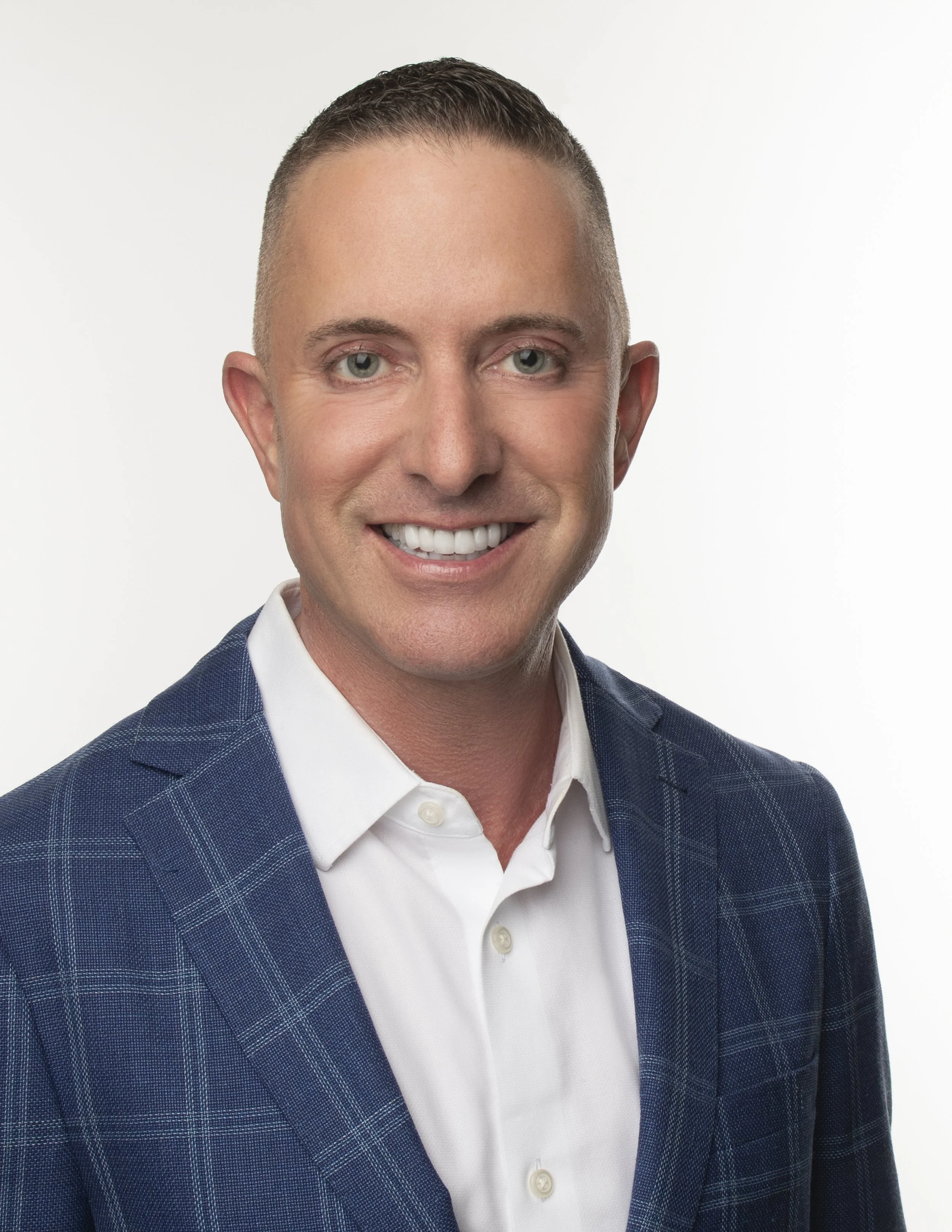 Headshot of a smiling man in a white shirt and blue plaid blazer against a white background.