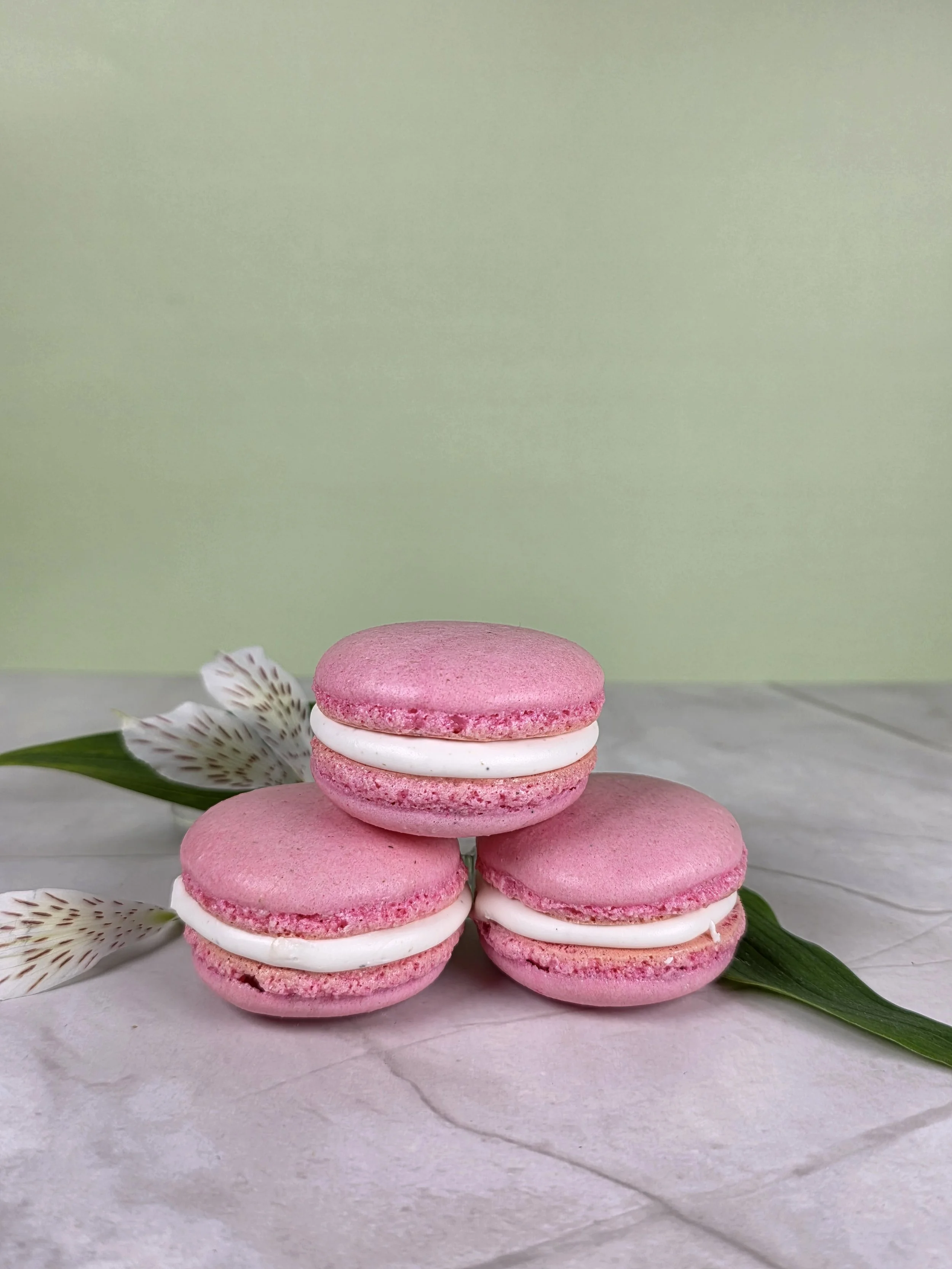 A bright pink trio of macarons with lovely white creme filling, sitting in a small pyramid atop marble with flower petals in the background
