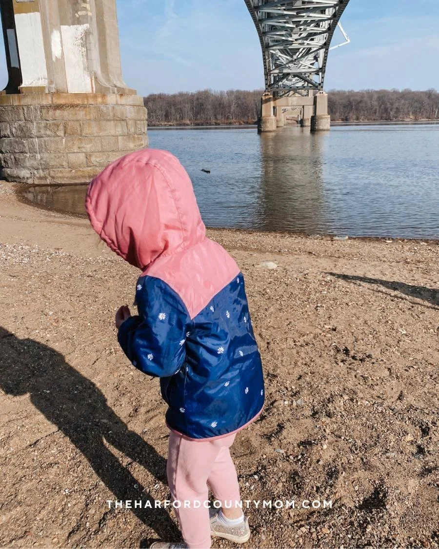 Girl wears jacket with hood up along Joe K's trail in Havre de Grace, Maryland. The trail is along the Susquehanna River with a bridge above