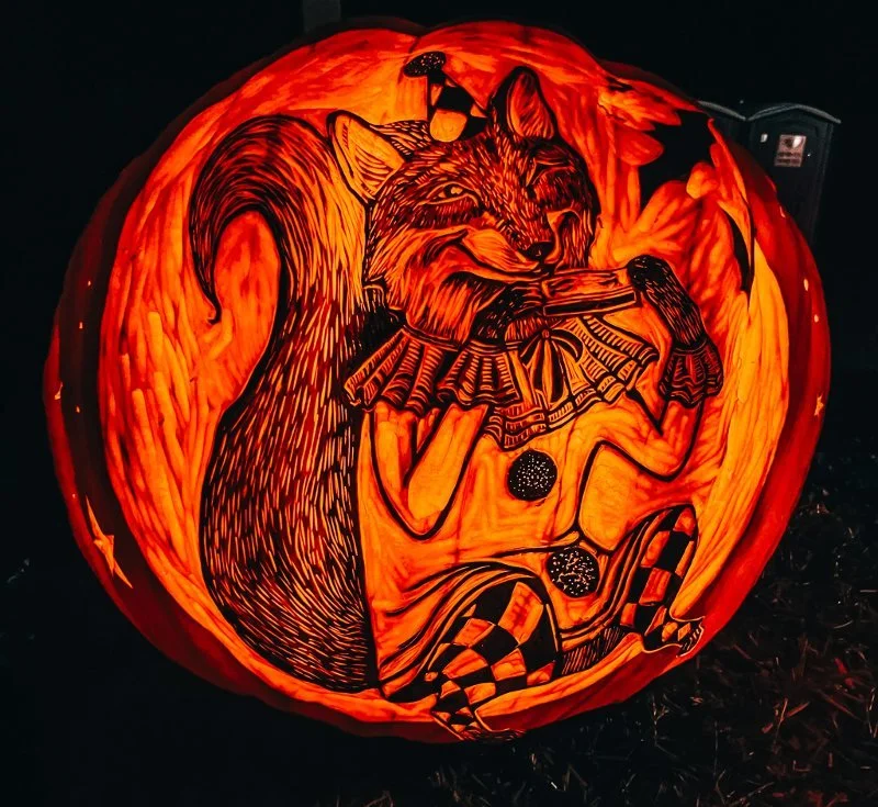 a pumpkin glowing with a detailed design carved into it to resemble a fox playing a harmonica from garden glow at ladew gardens