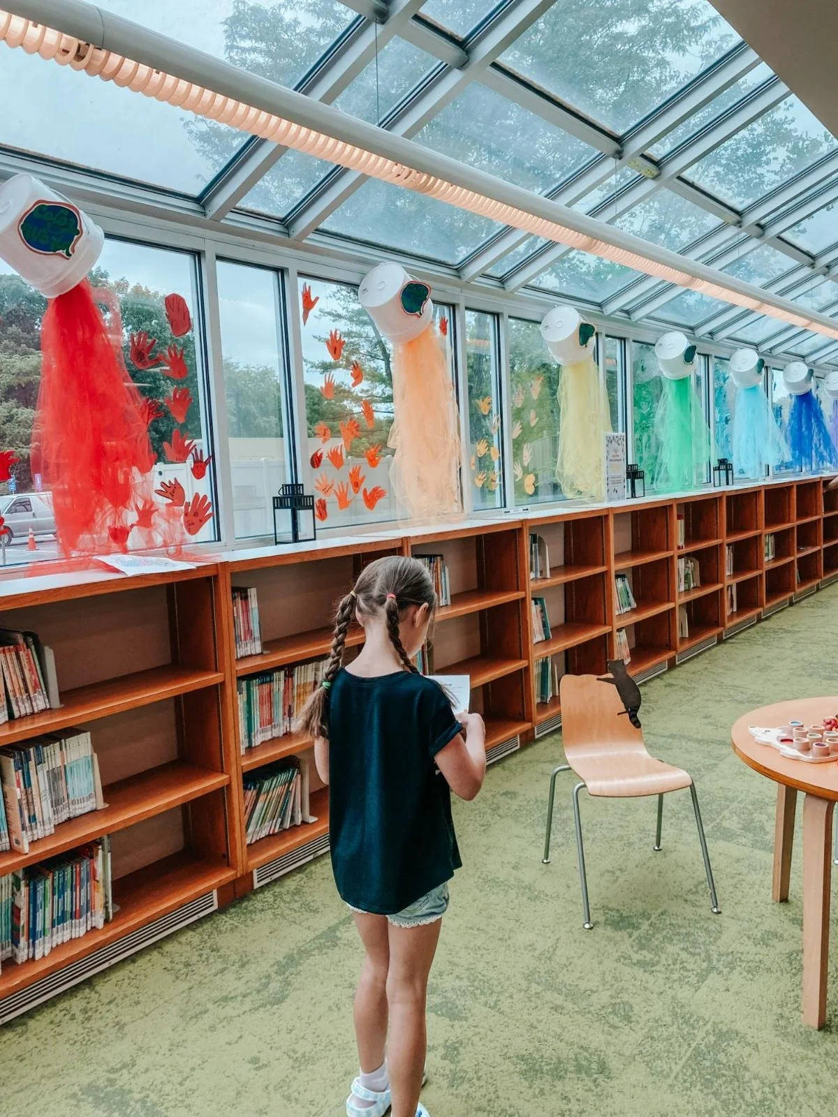 Girl looks down at scavenger hunt paper at Bel Air Library during the "Color Your World" summer reading campaign. Buckets of colors pour from the ceiling