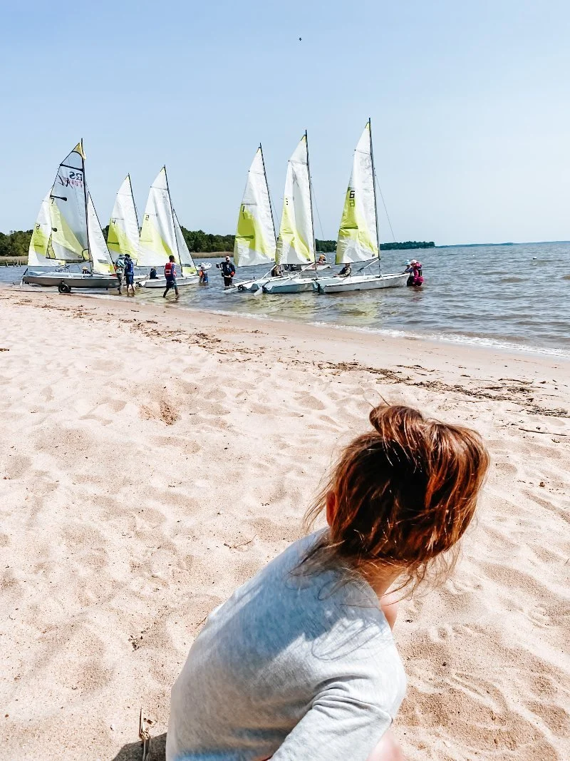girl staring at sail boats while playing on the beach at rocky point park in baltimore county