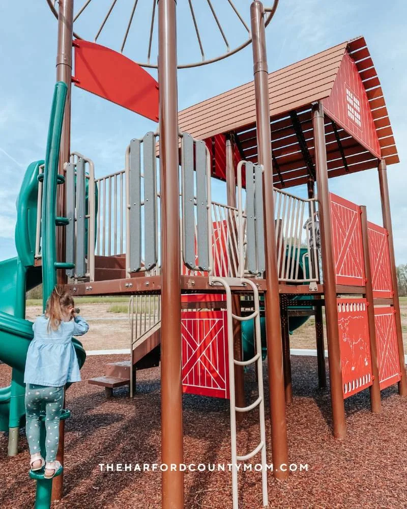 Girl climbs barn-themed playground structure at Poplar Grove Park in Street, Maryland
