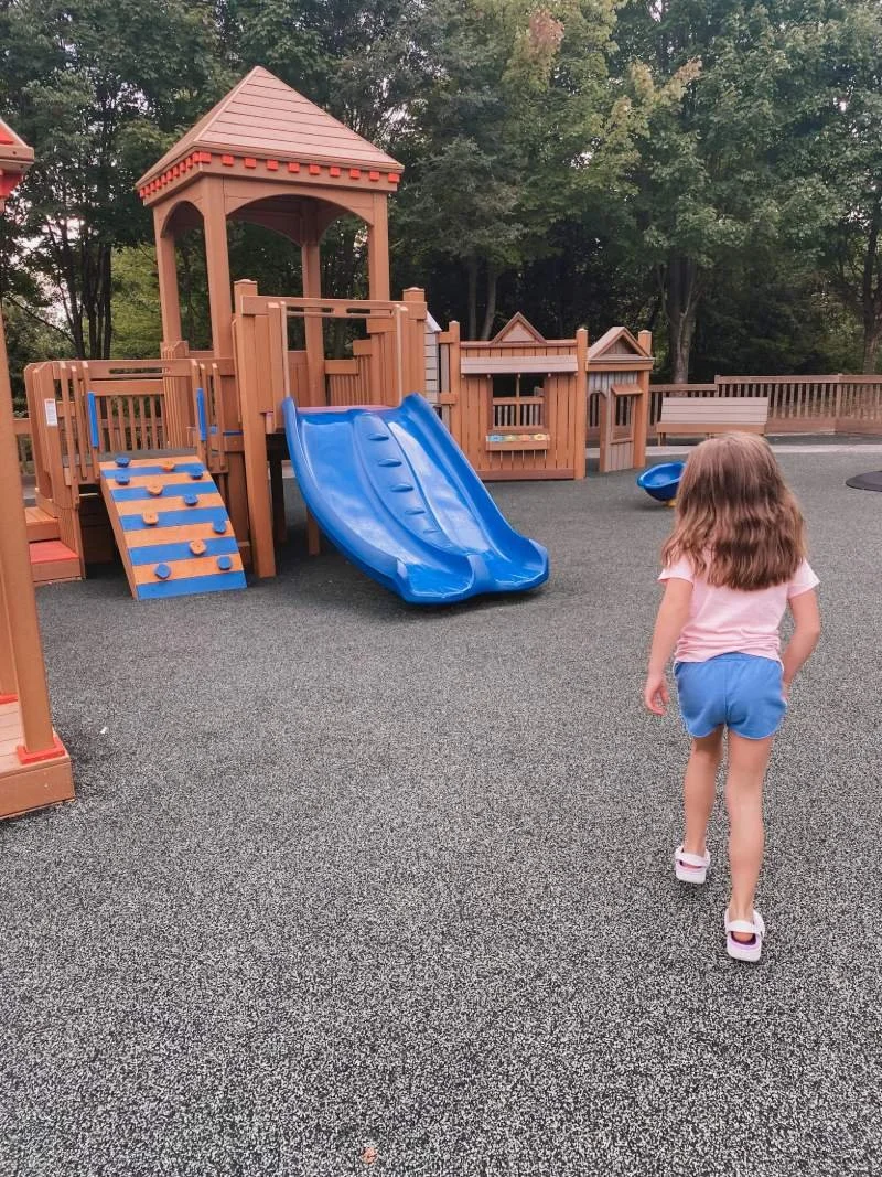 Girl runs towards toddler play area with smaller slides and climbing features at Getz Playground in Bel Air, Maryland