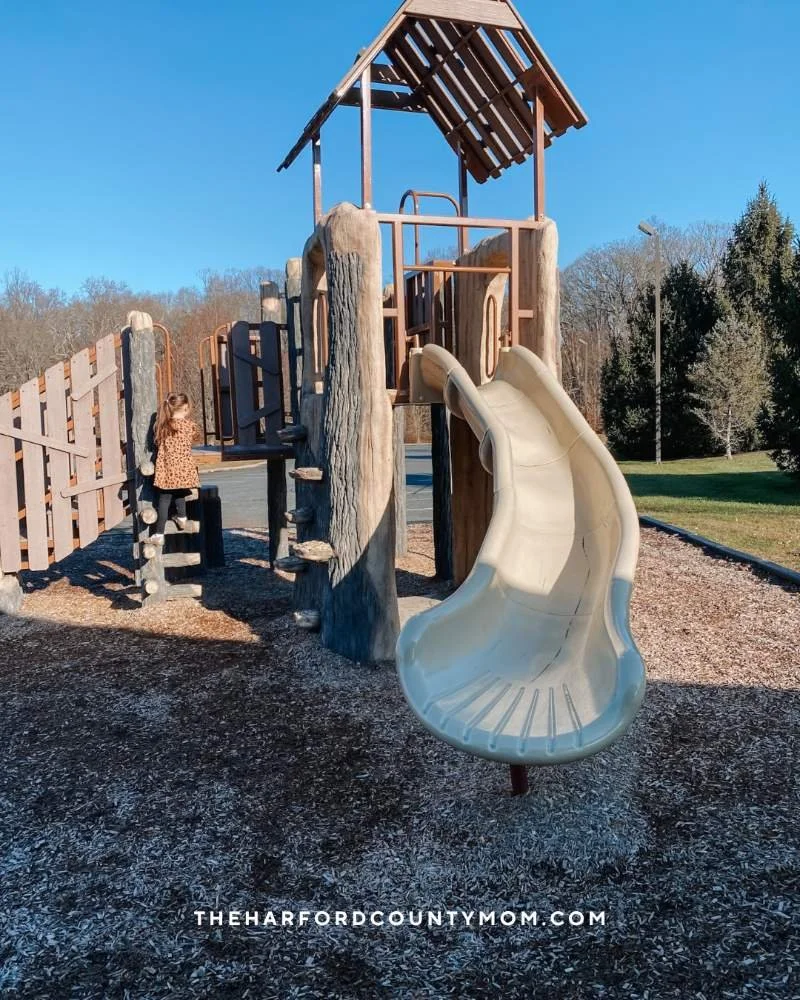 Girl climbs smaller play structure at Fox Meadows Park in Jarrettsville, Maryland that connects to a paved trail