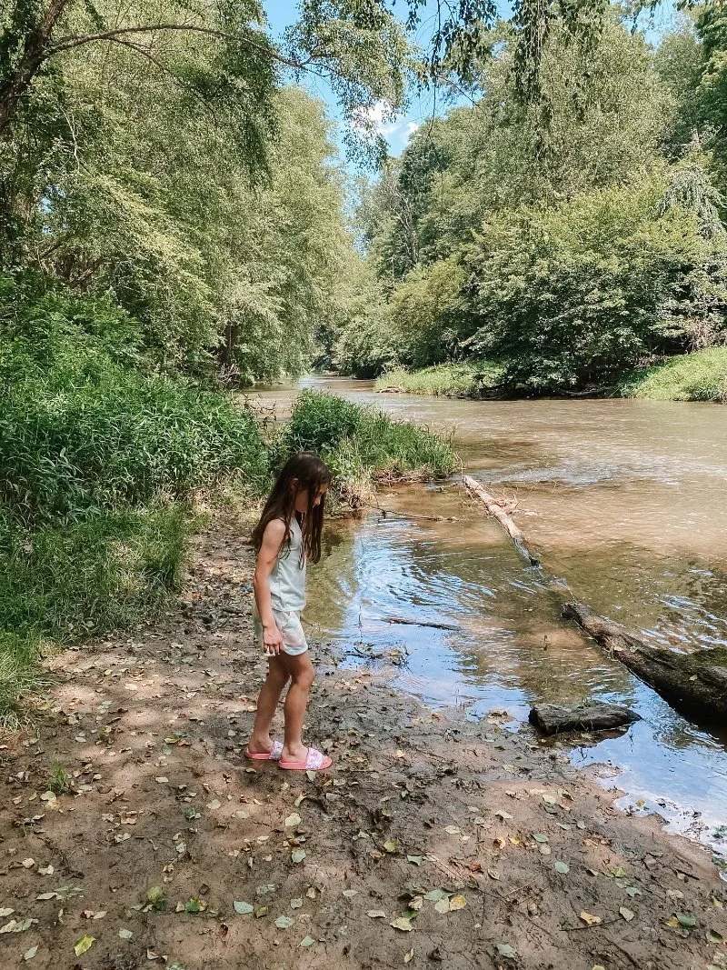 Girl overlooking the waters of Deer Creek, standing on a sandy beach at Eden Mill Park in Pylesville, MD