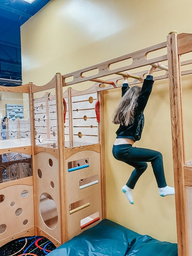 girl swinging on monkey bars at the playroom in forest hill