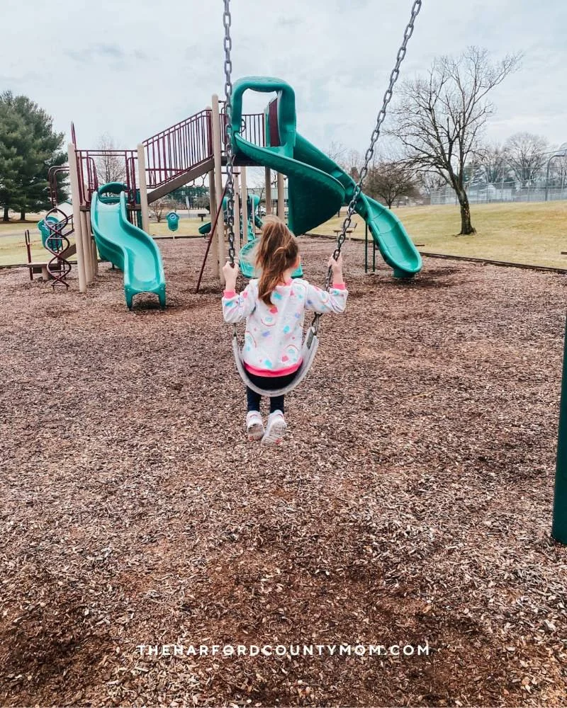 Girl swings with green play structure with slides in front of her at Francis Silver Park in Darlington, Maryland