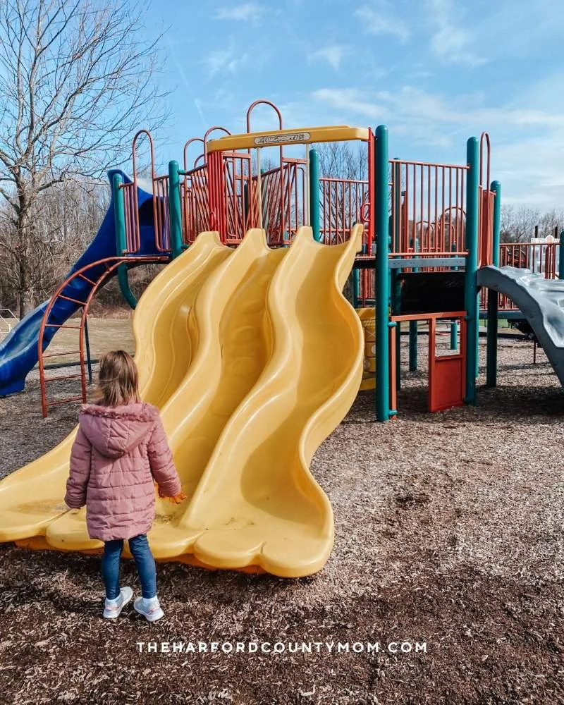 Girl walks towards yellow three-slide at Fallston Recreation Complex playground in Fallston, Maryland