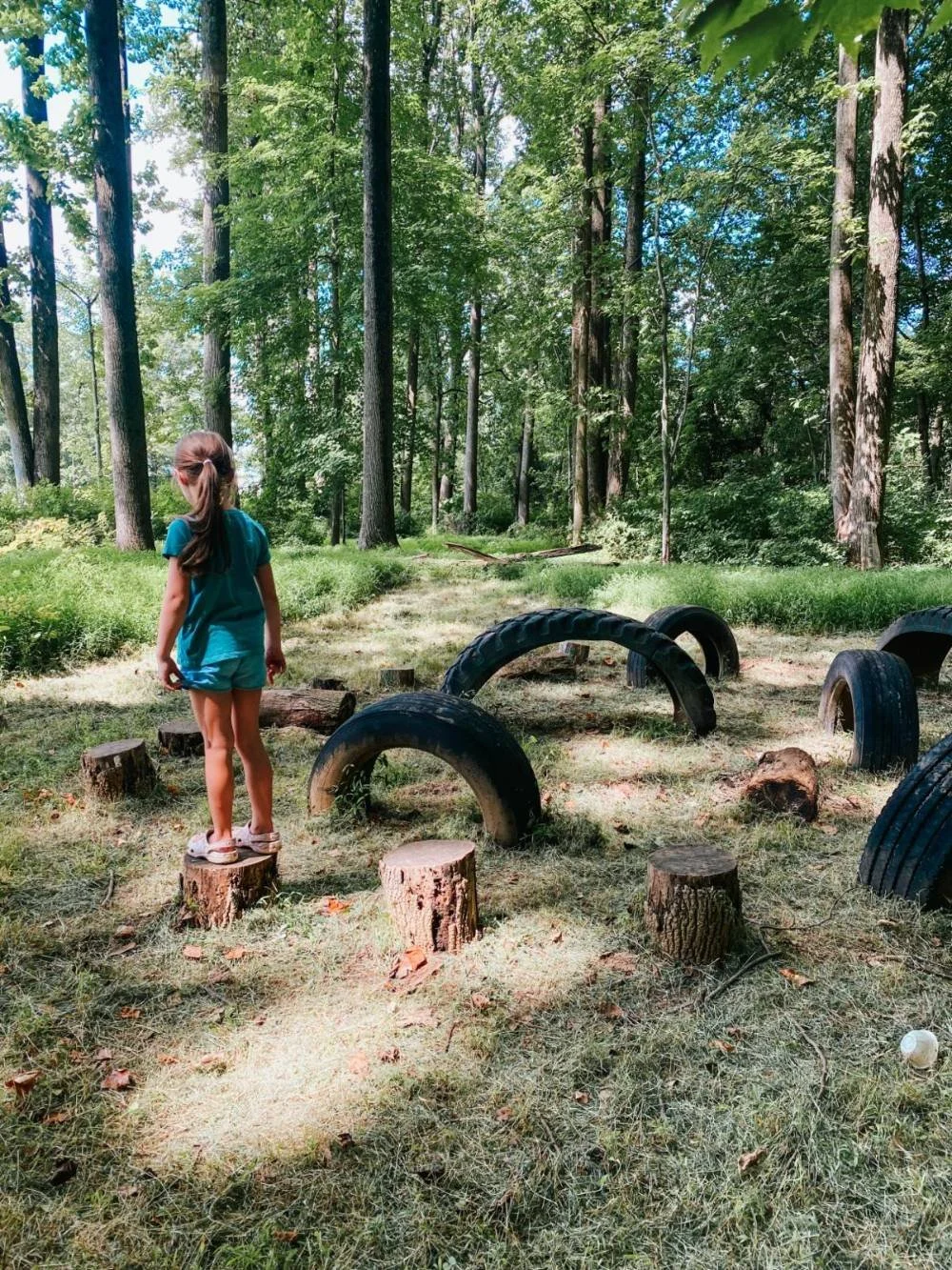 girl stands on tree stumps in obstacle course at Bear Legacy Trail in Abingdon, MD. See the Trail Guide for more info.