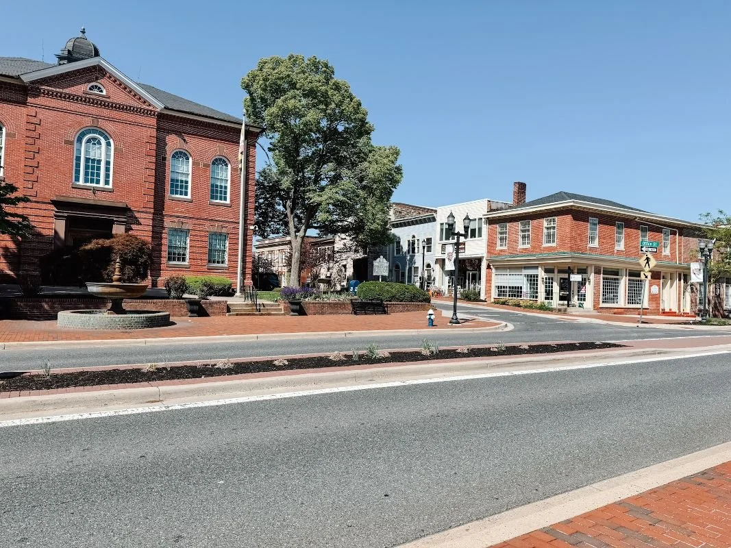 Street view of Downtown Bel Air, Maryland with brick buildings, trees, benches, street lamps, and a fire hydrant on a clear day.