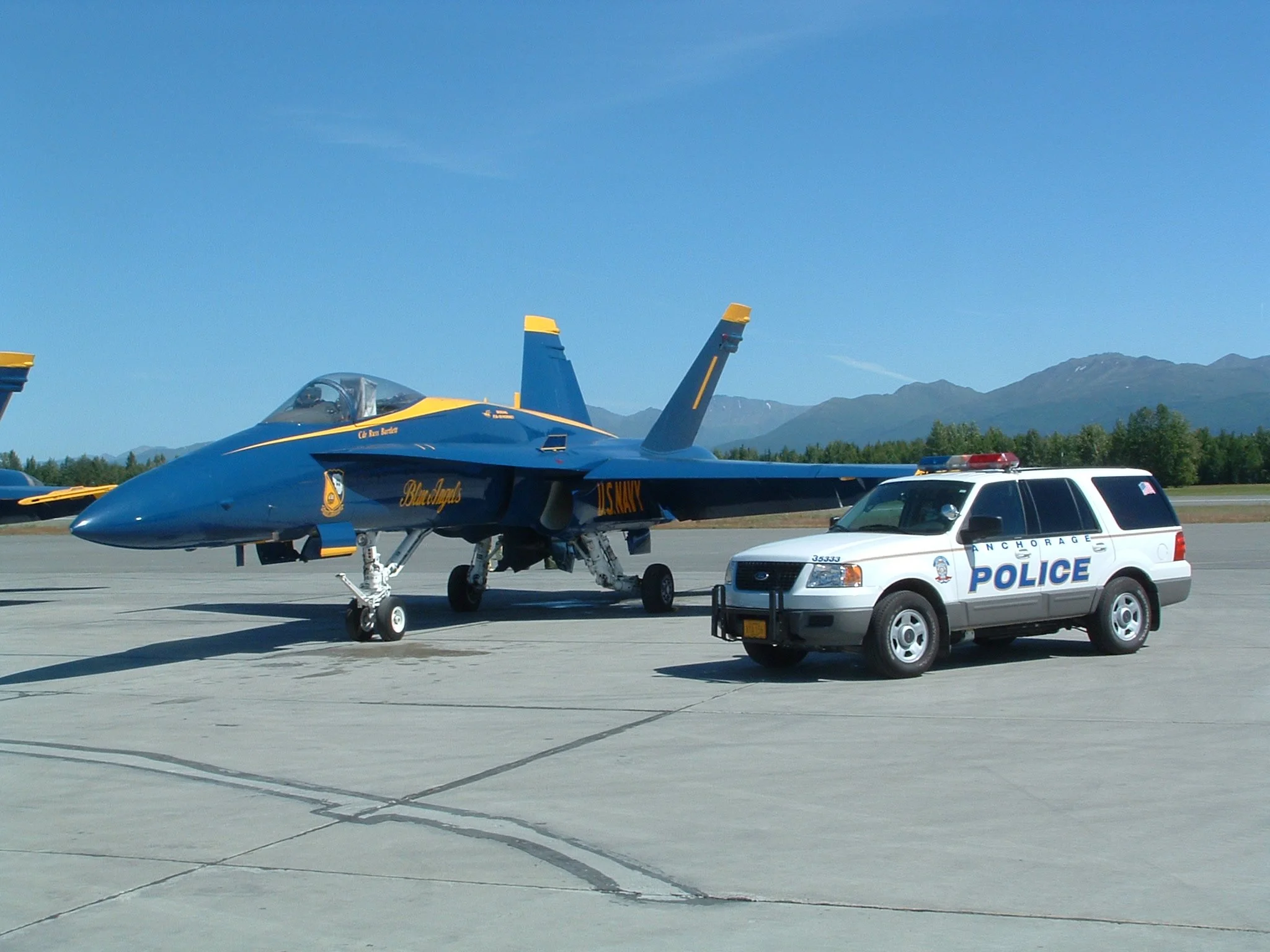 An image of an Anchorage Police Department patrol vehicle parked next to a US Navy Blue Angels F15 demonstration aircraft