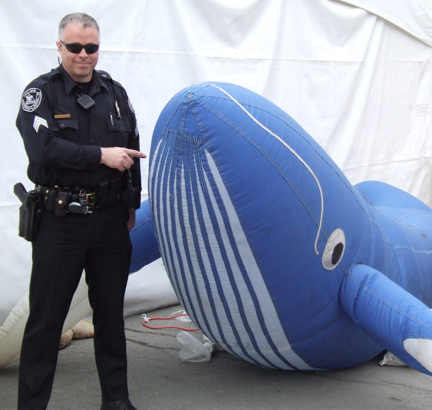 Image of Matt Bloodgood in his Anchorage Police Uniform, standing next to a blue whale balloon