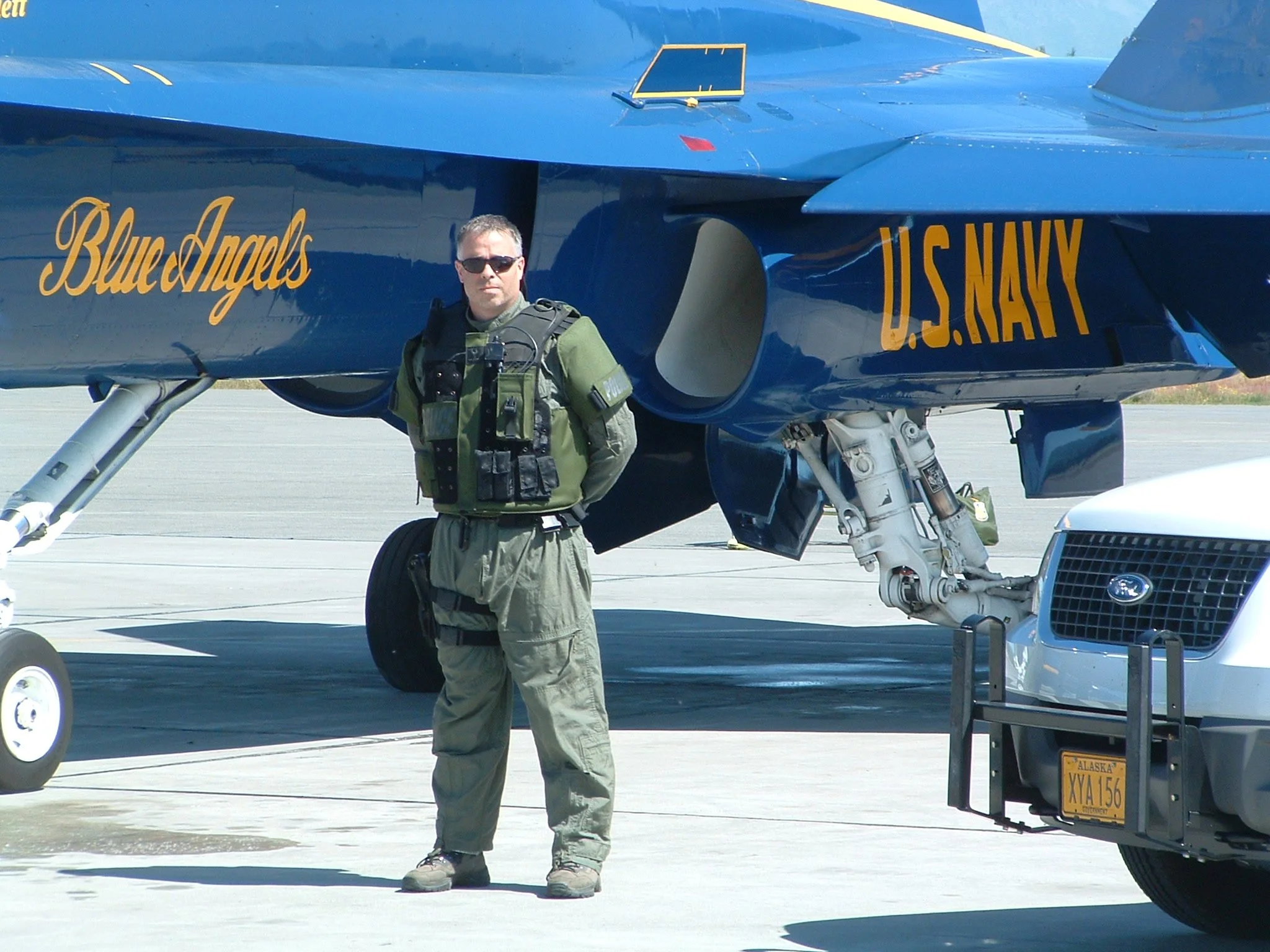 Police officer in green uniform standing next to a blue US Navy Blue Angels F15 aircraft