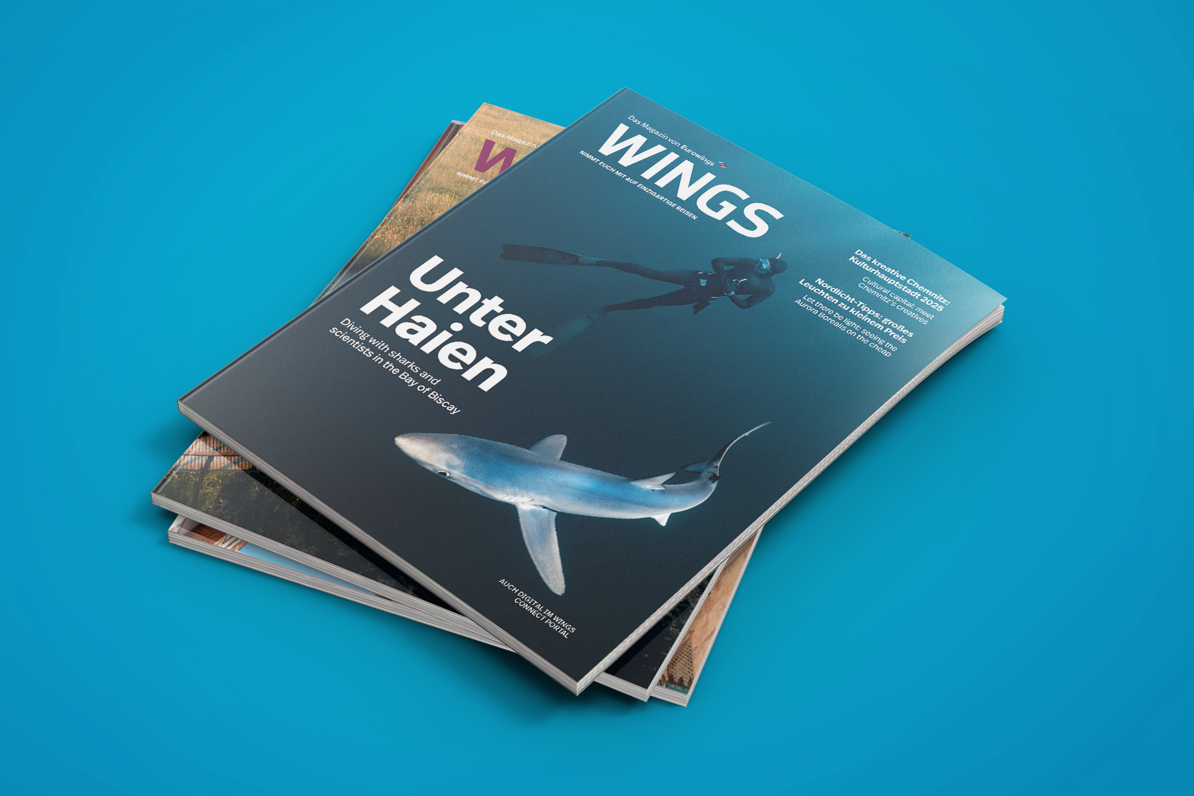 Stack of magazines, with the top magazine titled 'WINGS', featuring a diver in a wetsuit and a shark on the cover, against a blue background.